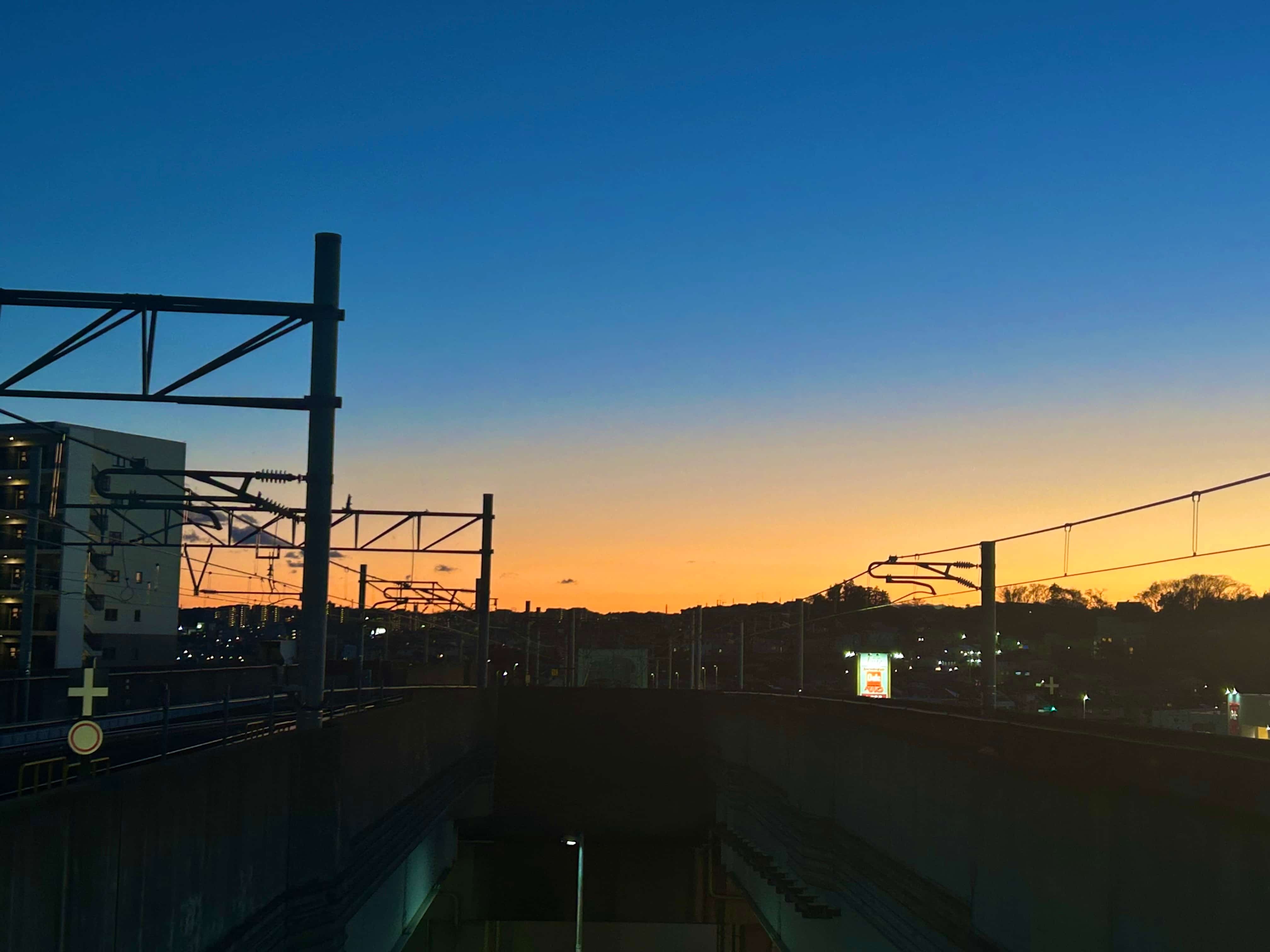 駅のホームから見える夕焼け空とシルエットの街並み